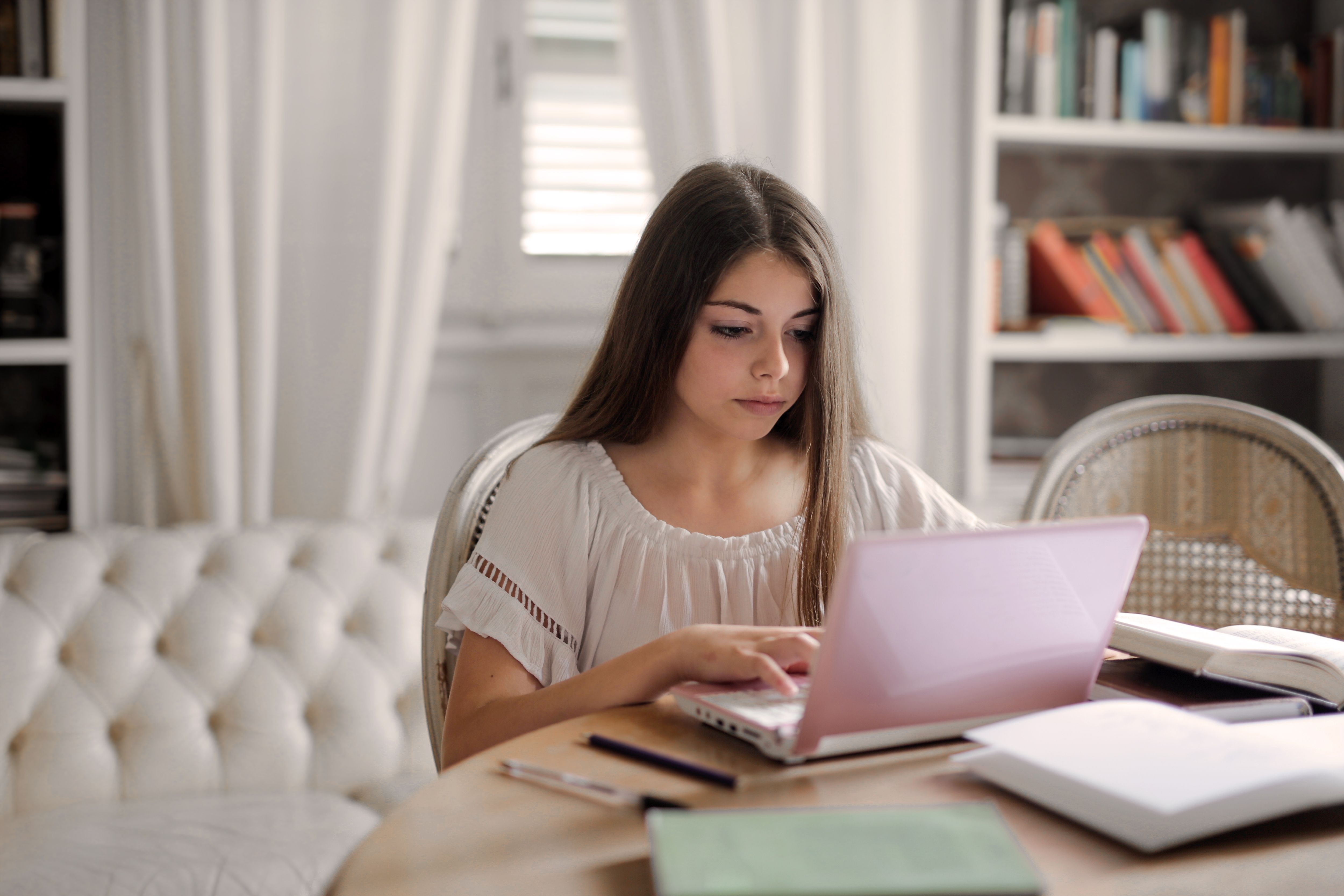 A young woman focused on studying with her laptop in a well-lit, cozy room setting.