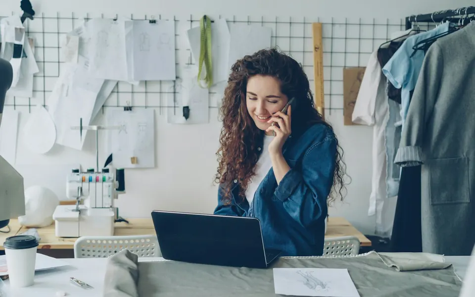 Selbstständige Designerin telefoniert in ihrem Atelier am Laptop