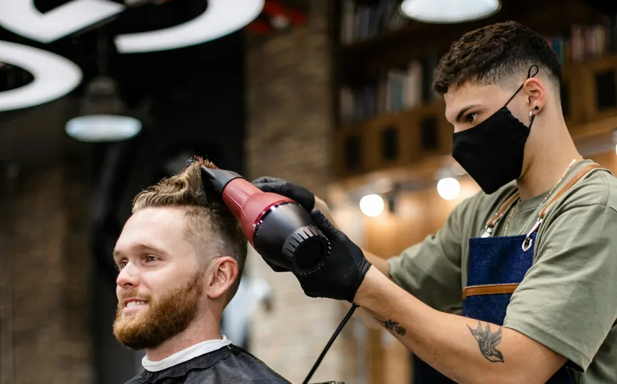 Friseur föhnt einem Kunden im Salon die Haare