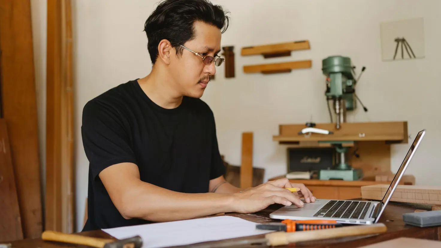 Handwerker sitzt in seiner Werkstatt am Tisch und arbeitet am Laptop